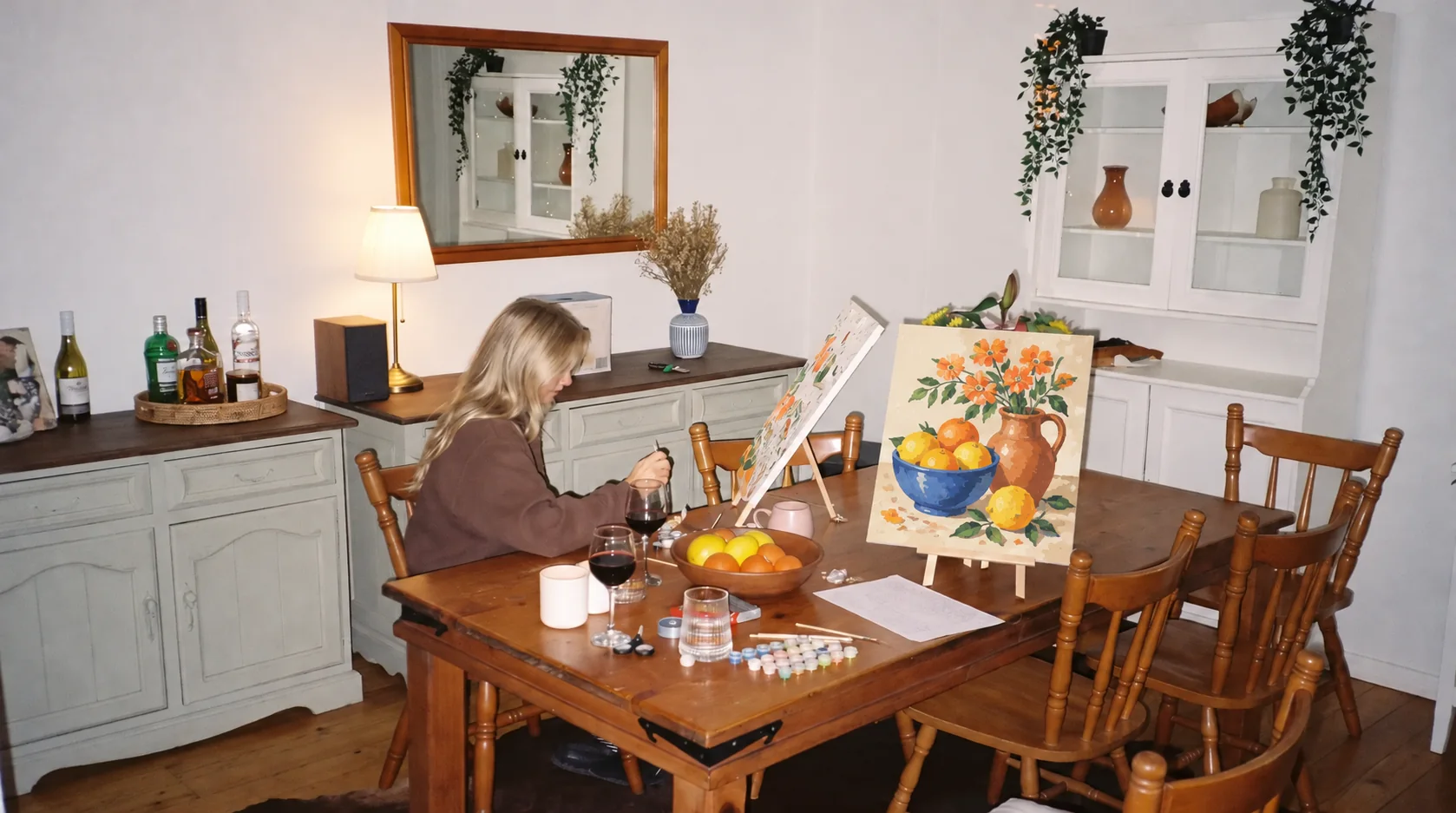 Mujer pintando un cuadro de flores y fruta por números en la mesa del comedor